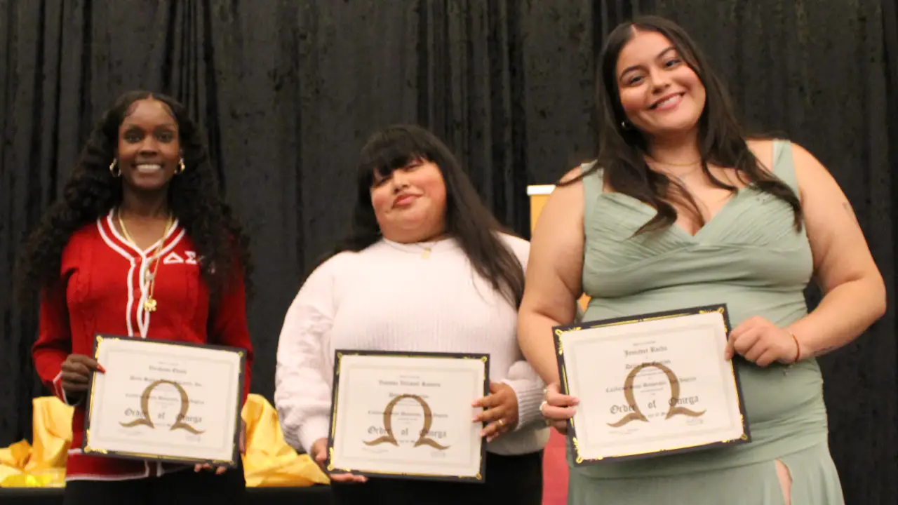 Three women on stage smiling and holding framed leadership awards